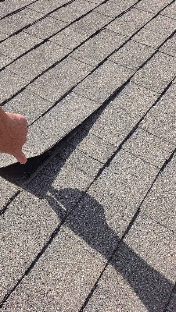 Hand lifting a loose shingle, a common roof repair