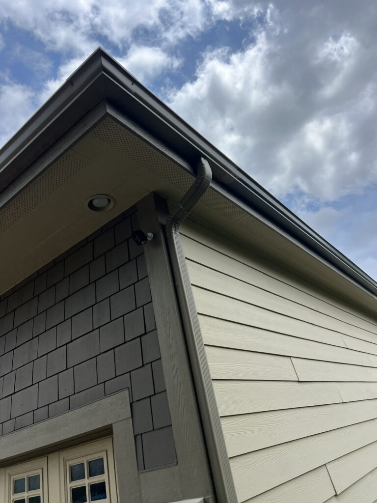 Seamless gutter corner and downspout on a home with gray shake and lap siding