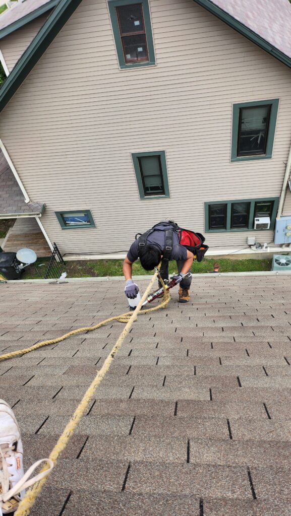 Wolf Roofing roofer tied off with a safety rope on a steep shingle roof