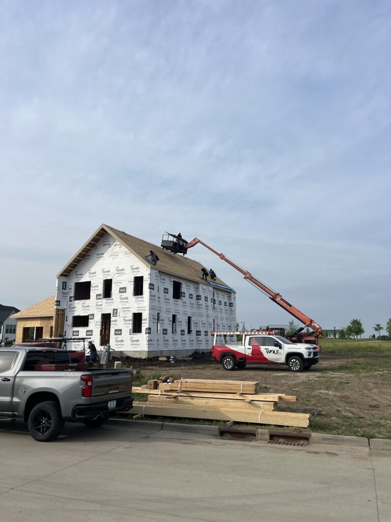 Wolf Roofing truck and boom loading shingles at a new construction job site